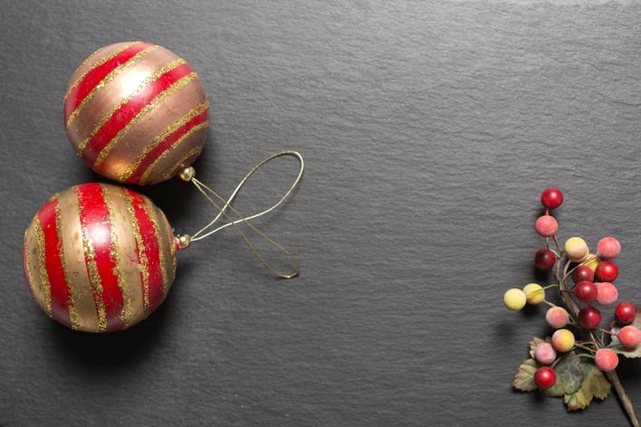 Two red and gold Christmas baubles on a dark slate surface